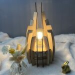 Lampe en bois dubaï, couleur brute avec sa propre ampoule. Posée sur une nappe en velour à côté d'un lapin 3D et d'un vase avec des fleurs en bois