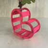 Décoration coeur "Adoration" en bois en rose. C'est un coeur qui accueil en son centre un petit vase pour y mettre des fleurs. Le coeur est un peu décalé et en plan serré.