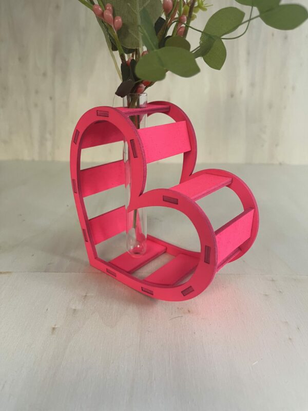 Décoration coeur "Adoration" en bois en rose. C'est un coeur qui accueil en son centre un petit vase pour y mettre des fleurs. Le coeur est un peu décalé et en plan serré.