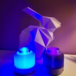 Lampes SOLEA LED devant un lapin en matière transparent. Le vase à gauche est de couleur blanc et celui de droite est un dégradé violet avec des paillettes. Les vases éclaire autour d'eux grâce à une led en dessous du vase.