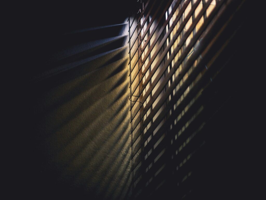 Volets à moitié fermés qui laisse passer les rayons du soleil dans une pièce sombre. Astuce pour éviter les grosses chaleurs dans notre maison